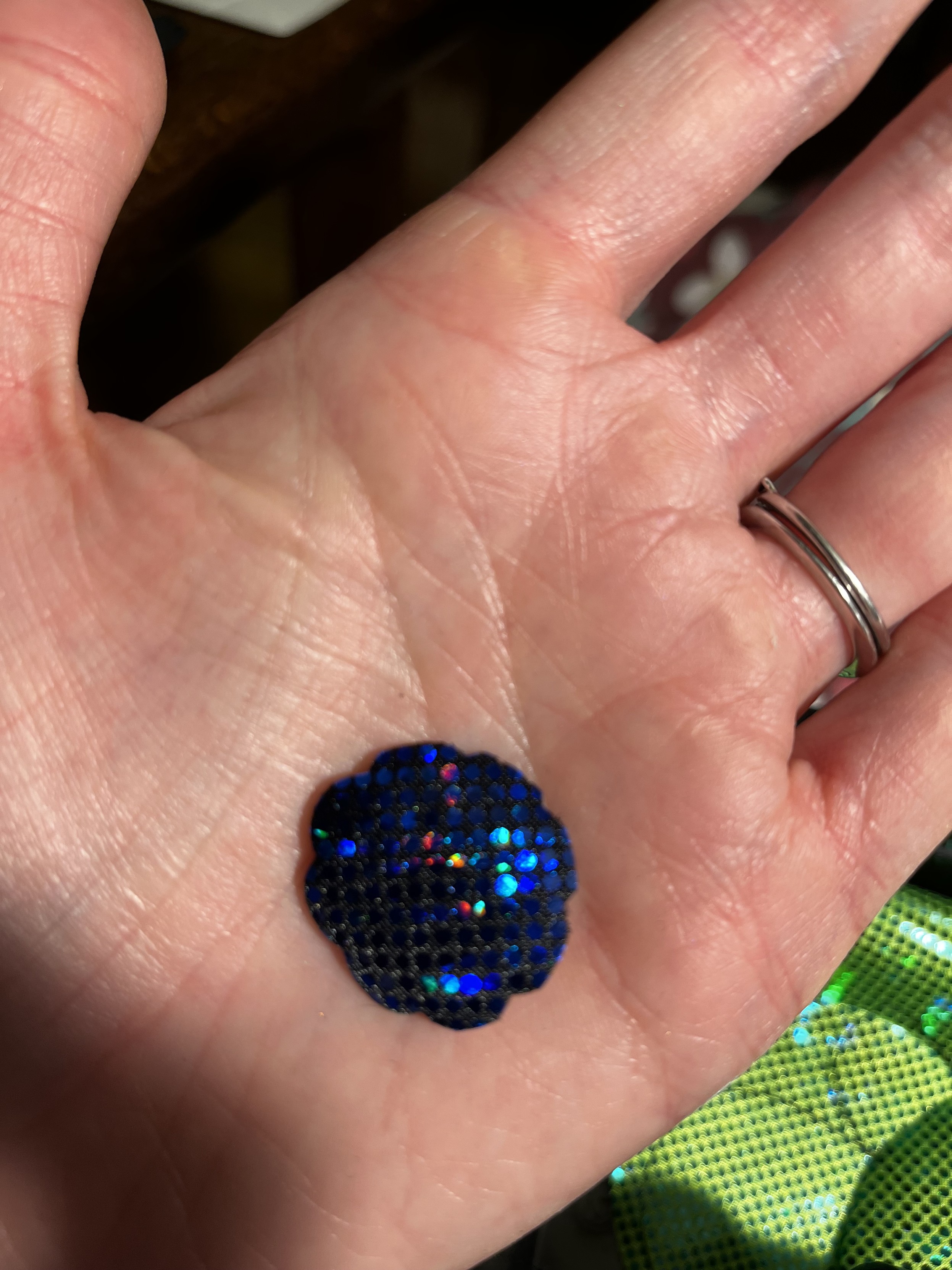 A small subtle flower shape cut from blue and black sparkly fabric, held in a woman’s hand. It’s about 1” across.