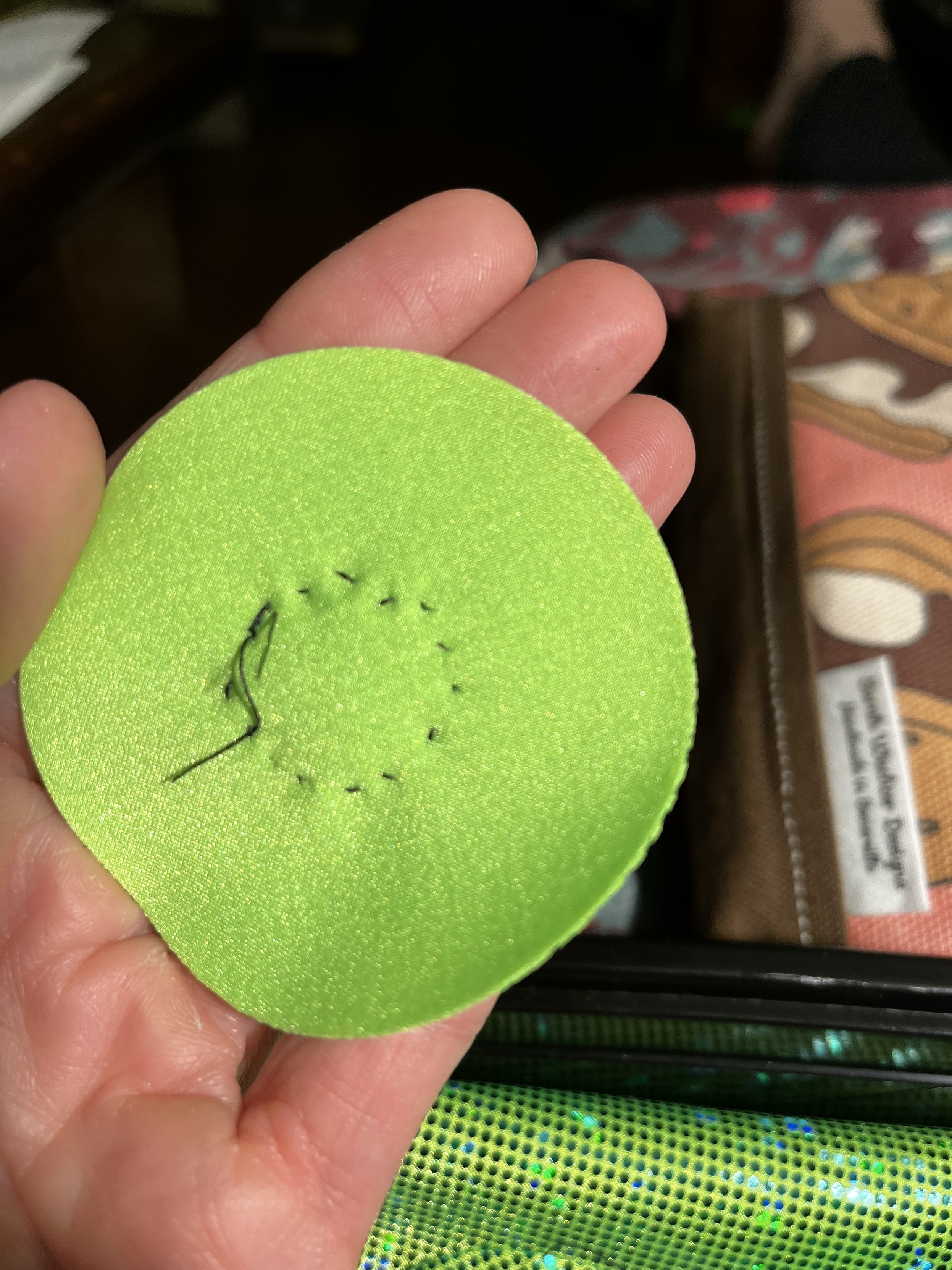 The backside of a round green patch showing the stitching around the pupils