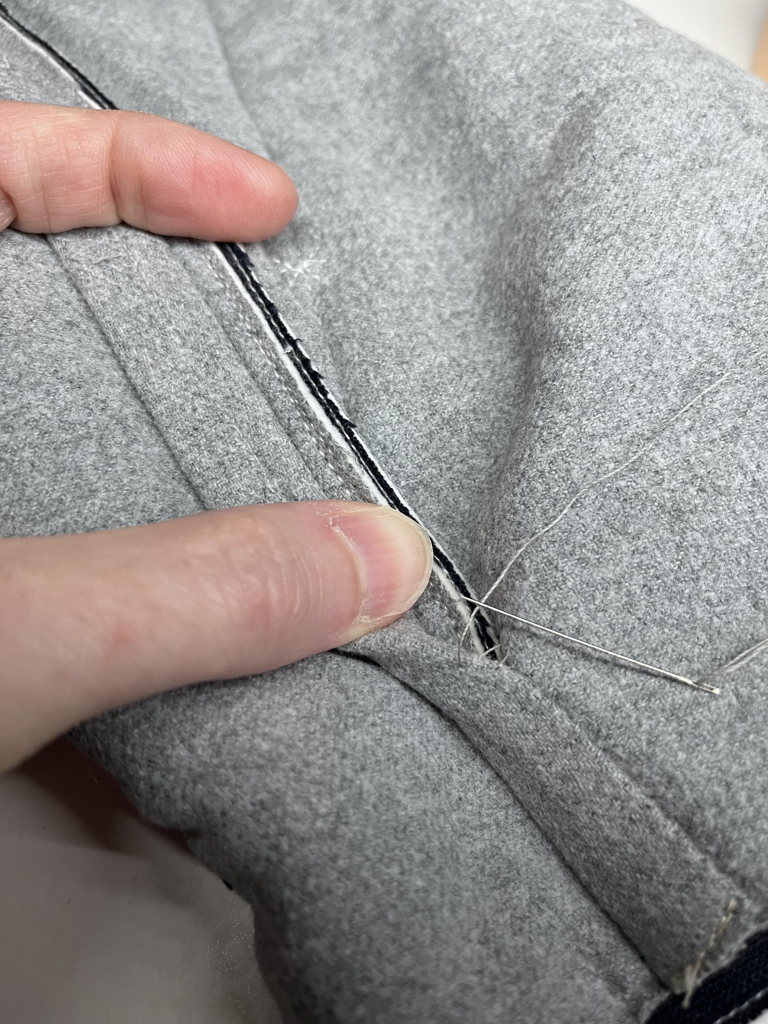 A Caucasian woman’s hand is holding down the seam allowance on a grey flannel quilt coat. You can see that the allowance for the two pieces is trimmed at a different width, with the top one being slightly narrower. A machine stitched line runs just inside the trimmed edge to compress the quilt.